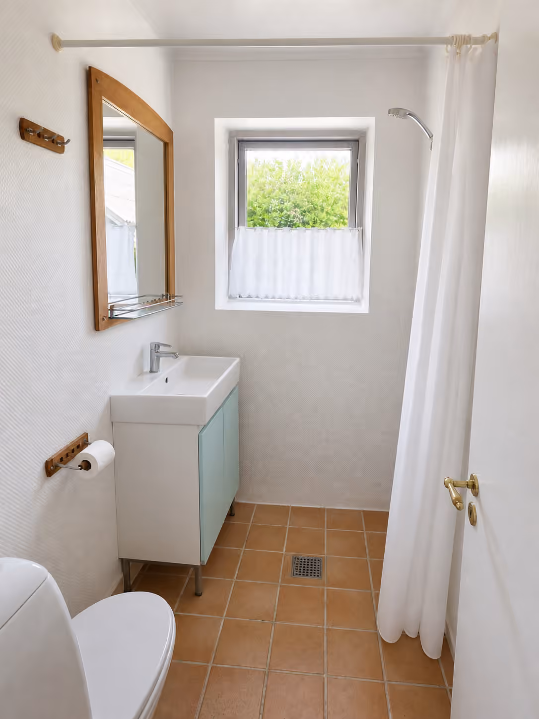 Det kompakte badeværelse i hovedhuset med bruser, håndvask og toilet.