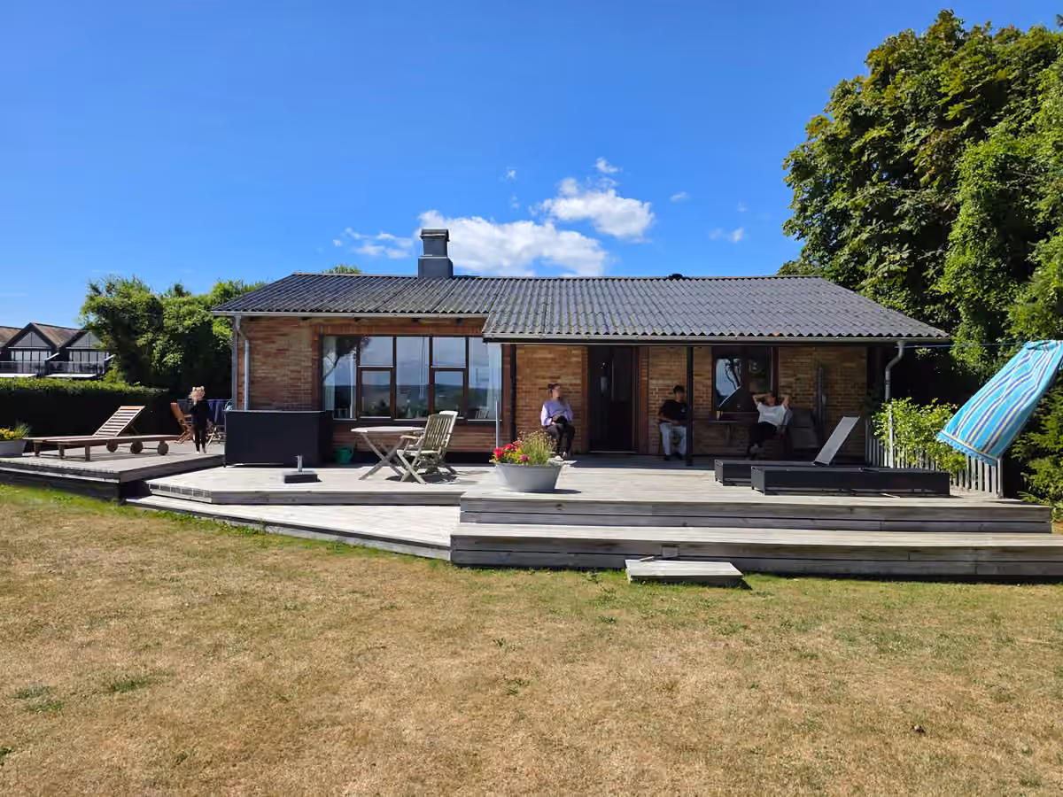 Hovedhusets murstensfacade og brede træterrasse i solskin